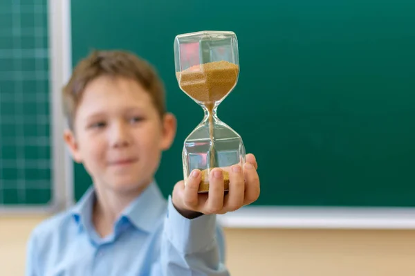 Op de palm van je hand, tegen de achtergrond van een schoolbord met de inscriptie terug naar school, zachte focus, is er een zwarte wekker. Terug naar schoolconcept. — Stockfoto