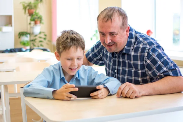 A father shows his son how to use the phone for distance learning. Back to school concept.