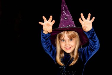  Siyah arka planda, kafasında kocaman bir şapka olan küçük cadı. Çocuk seni korkutmak istiyor. Cadılar Bayramı kostümü..