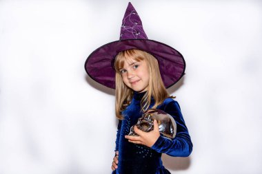  Beyaz arka planda, kafasında kocaman bir şapka olan küçük cadı. Kızın elinde gümüş bir kafatası var. Cadılar Bayramı kostümü.