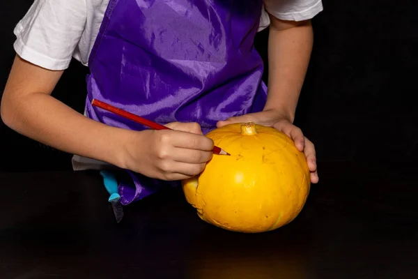 Un niño dibuja una cara aterradora en una calabaza. Feliz Halloween. — Foto de Stock