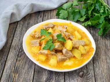 Ahşap arka planda et ve sebzeli ev yapımı güveç, gri keten havlu ve maydanoz. Lezzetli ve besleyici bir yemek. Patates, havuç ve baharatla pişirilmiş domuz eti, Macar kebabı.