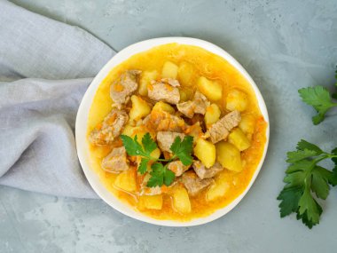 Romanya mutfağı - taze ev yapımı et ve maydanozlu patates. Ahşap zemin üzerinde domuz eti ve sebzeli güveç ve gri keten havlu. Lezzetli ve besleyici bir yemek..