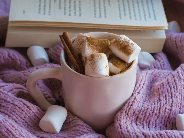 Acogedor, humor, estilo de vida, concepto de naturaleza muerta. Taza de café de cacao aromático con malvaviscos, suéter y canela en suéteres de punto rosa como fondo. Bebida caliente tradicional de invierno u otoño en casa. — Foto de Stock