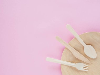 Tabak ve mutfak gereçleri pembe kağıt arka planda ahşap, biyolojik olarak çözünebilir tabaklar. Çevre dostu seçim ve doğa dostu. Plastiksiz ve temiz bir gezegen kavramı. Metin için boşluk
