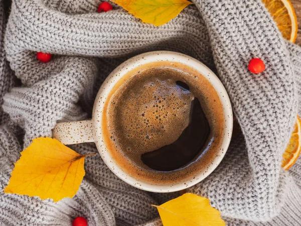 Sonbahar mı sonbahar mı sabah kahvesi mi? Sonbahar sarı yaprakları, kırmızı Rowan meyveleri, arka plan olarak sıcak dumanı tüten koyu kahve kupası ve rahat gri bir kazak. Pazar rahatlatıcı, sonbahar havası ve durgun hayat konsepti..