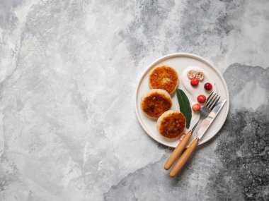 Kahvaltıda sağlıklı peynirli kek. Beyaz tabakta süzme peynirli krep, ekşi krema ve gri arka planda böğürtlen. Ev yapımı geleneksel Ukrayna ve Rus şurubu. Kopyalama alanı olan üst görünüm