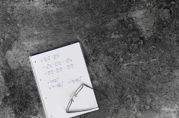 mathematics book with calculation tasks, glasses, on a grey marble table