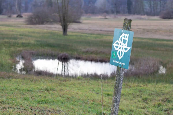 german nature conservation area shield in front of a moor landscape with a small lake in the background, german text translation: nature conservation area