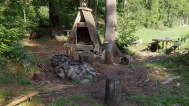Boş pirinç tenceresi ve boş siyah ızgarası olan bir şömine, gri taşlar ve kahverengi orman zeminleri arasında gri bir kova, şömineler yürüyüşçülere gündüz yemek pişirecek bir yer sunuyor.