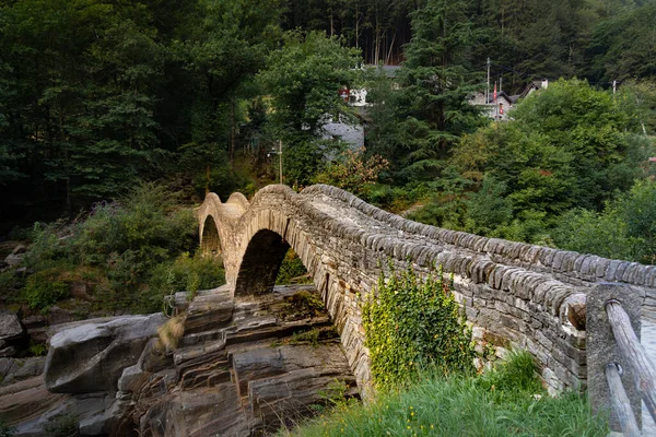 people empty rustic roman bridge in ticino, warm sunset, bright green forest with ticino stone houses, the famous bridge is a destination for many tourists from around the world, by day