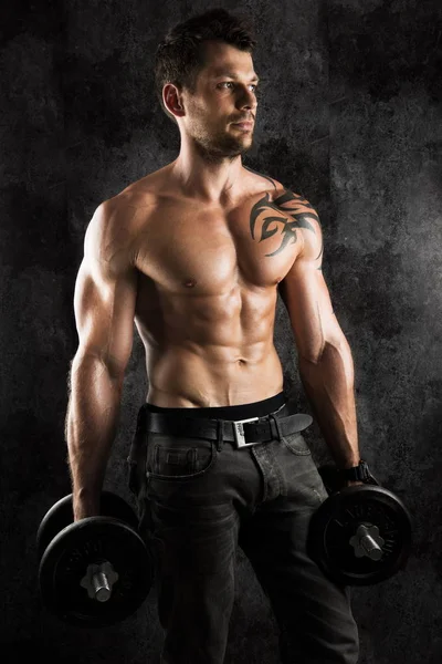sexi vücut geliştirmeci atelier dumbbells ile siyah artalanları üzerinde poz kas ile