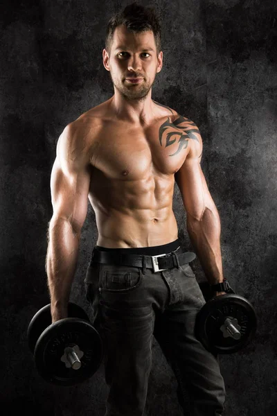 sexi vücut geliştirmeci atelier dumbbells ile siyah artalanları üzerinde poz kas ile