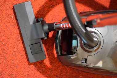 Elinde fırça ve çanta olan bir elektrikli süpürge. Kırmızı halıda elektrikli süpürge..