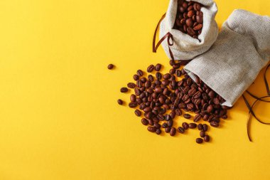 Kahve çekirdekleri kopya alanı metni sarı zemin üzerine torbalarda.