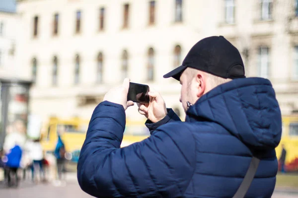 A fiatalember egy fekete sapkát fotózni egy emlékmű-val mozgatható telefon. Utazási koncepció. — Stock Fotó