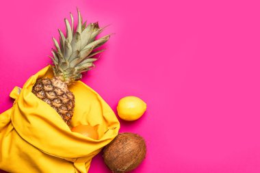 Pembe arka plan üzerinde sarı pamuklu çanta ile Tropikal meyveler.