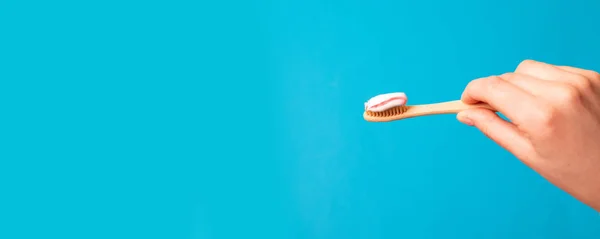 Mão feminina com pasta de dentes na escova contra fundo azul — Fotografia de Stock