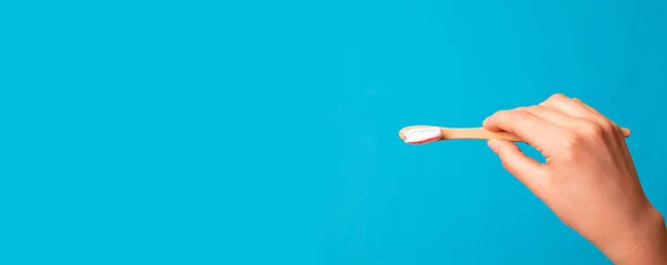 Mão feminina com pasta de dentes na escova contra fundo azul — Fotografia de Stock