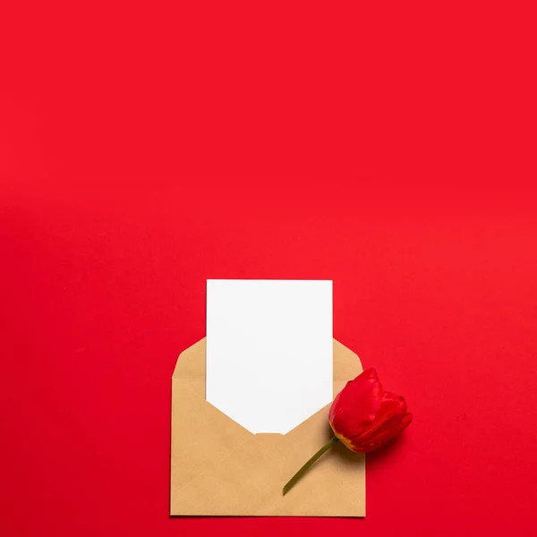 Minimalistische kaart mockup met rode tulp, ambachtelijke envelop, bloesem, platte lay, Top uitzicht — Stockfoto