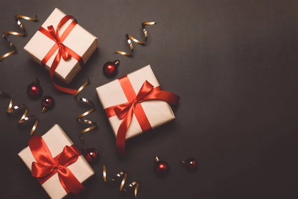 Regalos de artesanía navideña con cintas rojas y confeti de oro sobre un fondo de contraste oscuro —  Fotos de Stock