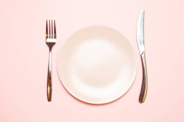Pembe bir masa örtüsü üzerinde çatal ve bıçak ile pembe boş plaka
