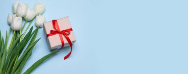 Paskalya günü geçmişi. Beyaz lale çiçek buketi üst görünümü, mavi arka plan üzerinde kırmızı bant ile hediye kutusu
