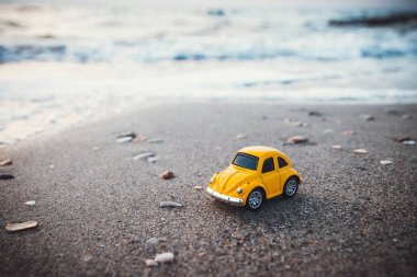 Yazın güneş ışığında kumsalda sarı oyuncak araba. Tatil ve seyahat kavramı.
