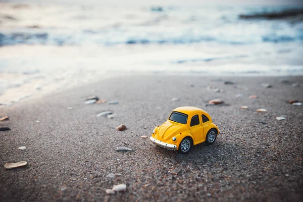 Yazın güneş ışığında kumsalda sarı oyuncak araba. Tatil ve seyahat kavramı.