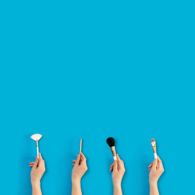 Mavi arka planda kadın ellerde makyaj fırçaları