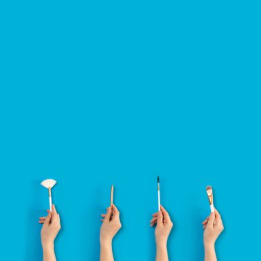 Mavi arka planda kadın ellerde makyaj fırçaları