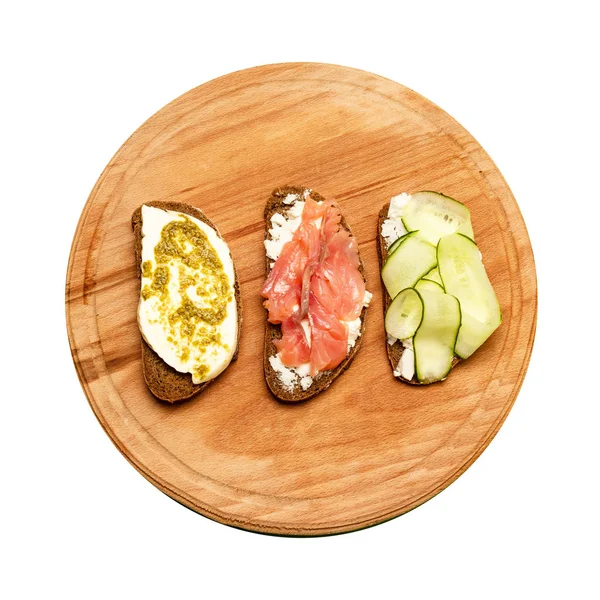 Petit déjeuner matinal de sandwichs assortis avec différentes garnitures sur une planche en bois. Sandwich au poisson avec fromage et concombre sur le fond . — Photo