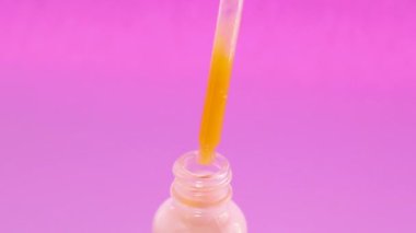 Pembe arka plan üzerinde bir pipet ile cam şişede doğal kozmetik. Kadın vücudu için bakım.