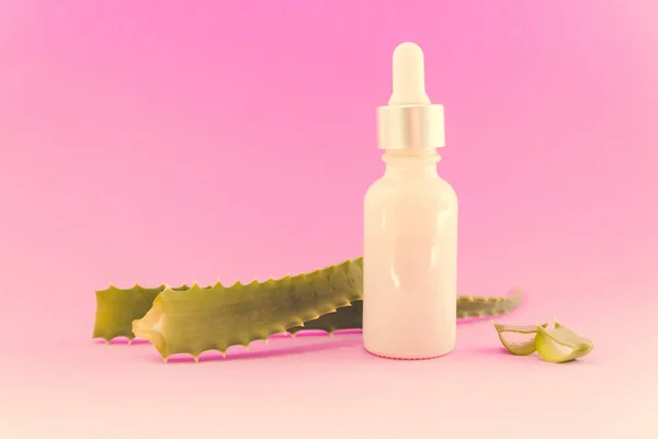 Косметическая или медицинская бутылка с пипеткой с листьями алоэ на розовом фоне — стоковое фото
