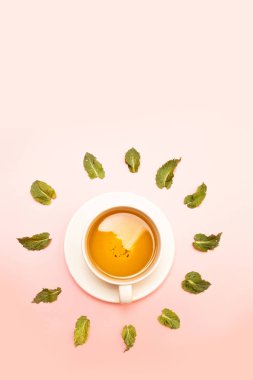 Pembe bir arka plan üzerinde nane yaprakları ile bitkisel yeşil veya siyah çay ile beyaz seramik fincan Yaratıcı kavramı.