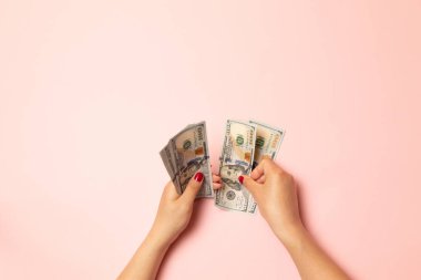 Kırmızı tırnaklı kadın pembe bir masada dolar demeti sayma, üst görünümü.