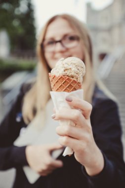 Genç sarışın kadın vanilya koni dondurma tutan ve bir doğa arka plan, sokak üzerinde kameralar a gülümseyen.