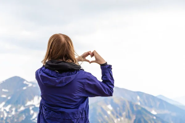 Młoda kobieta, która kształtuje serce z rękami patrzy na naturę zielonych wzgórz gór — Zdjęcie stockowe