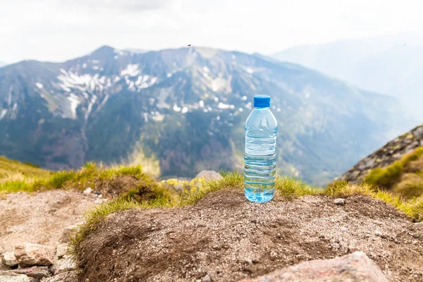 Helder water in een plastic fles staat op een steen hoog in de bergen op een zonnige dag. — Stockfoto