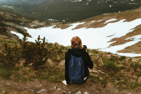 Молодая блондинка путешествует с голубым рюкзаком, сидит на вершине горы и наслаждается зелеными горными пейзажами. Вид сзади — стоковое фото