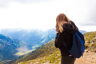 Siyah kazak ve tozluk genç kız dağlarda duruyor ve güzelliğin doğasını fotoğraflıyor. Seyahat ve bloglama konsepti.