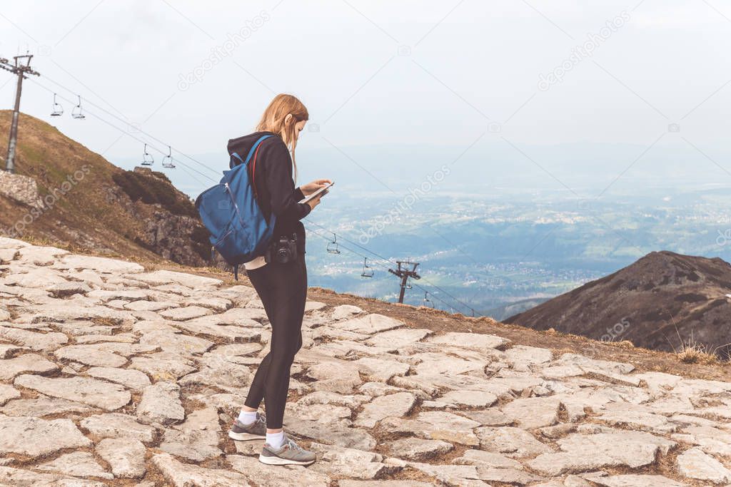 Young girl in a black sweater and leggings stands in the mountains and uses the phone