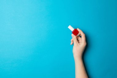 Womans el açık lacivert arka plan üzerinde kırmızı vernik ile bir şişe cam manikür tutar.