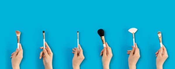 Cosmetic makeup brushes in a female hand on a blue background. — Stock Photo, Image