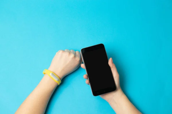 Fitness tracker on a woman hand on blue background and mock up of smartphone.