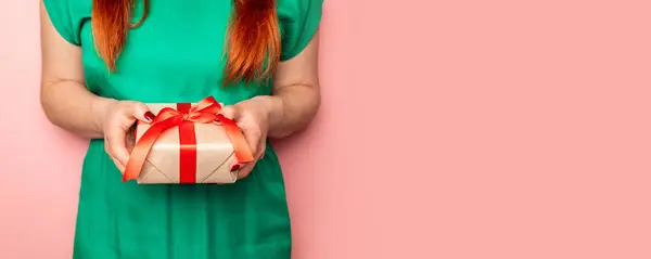 Flicka i en grön klänning håller i hennes händer en jul hantverk gåva överraskning med ett rött band — Stockfoto