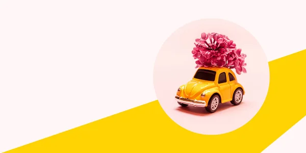 Міжнародний щасливий жіночий день. Іграшка жовта машина з бузковою квітковою гілкою на рожевому фоні з місцем для тексту. — стокове фото