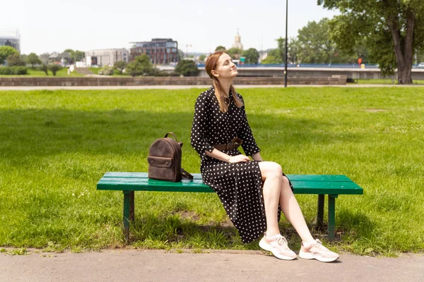 Самотня дівчина в сукні на лавці парку, насолоджується відпусткою . — стокове фото