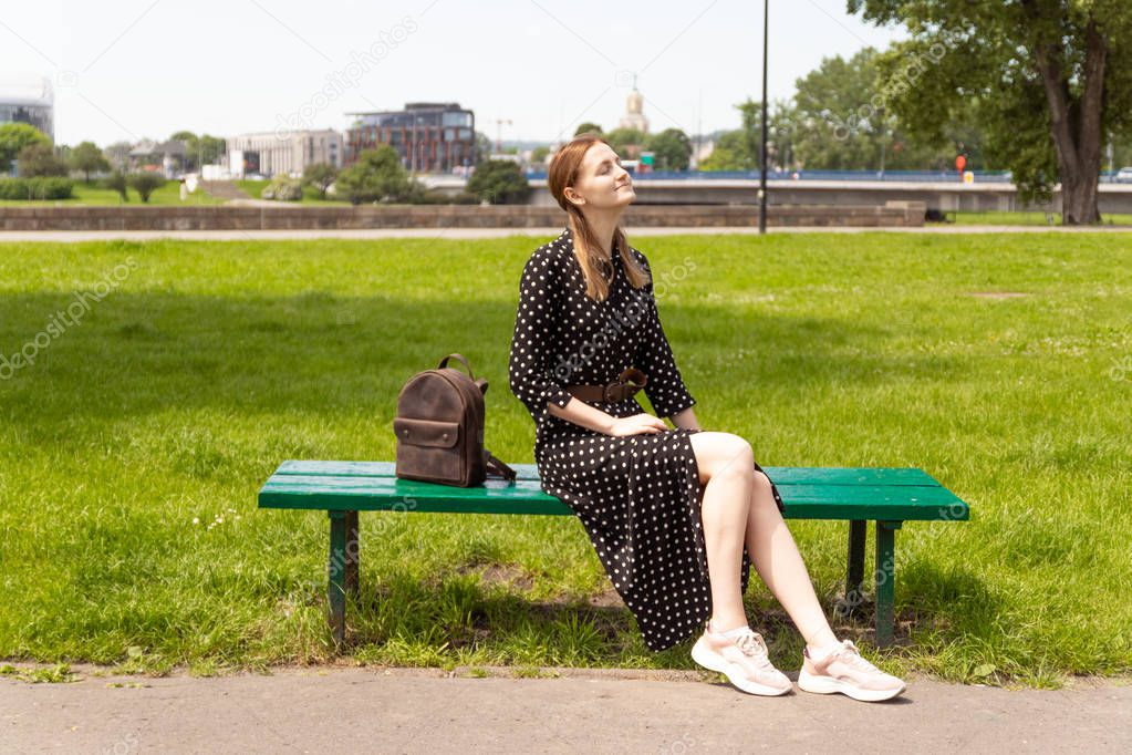 Lonely girl in a dress on a park bench, enjoys a vacation.