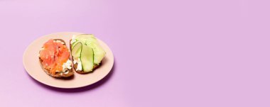 Kırmızı balık, beyaz peynir salatalık ve mor bir arka plan üzerinde pembe seramik plaka üzerinde pesto ile lezzetli taze sandviç
